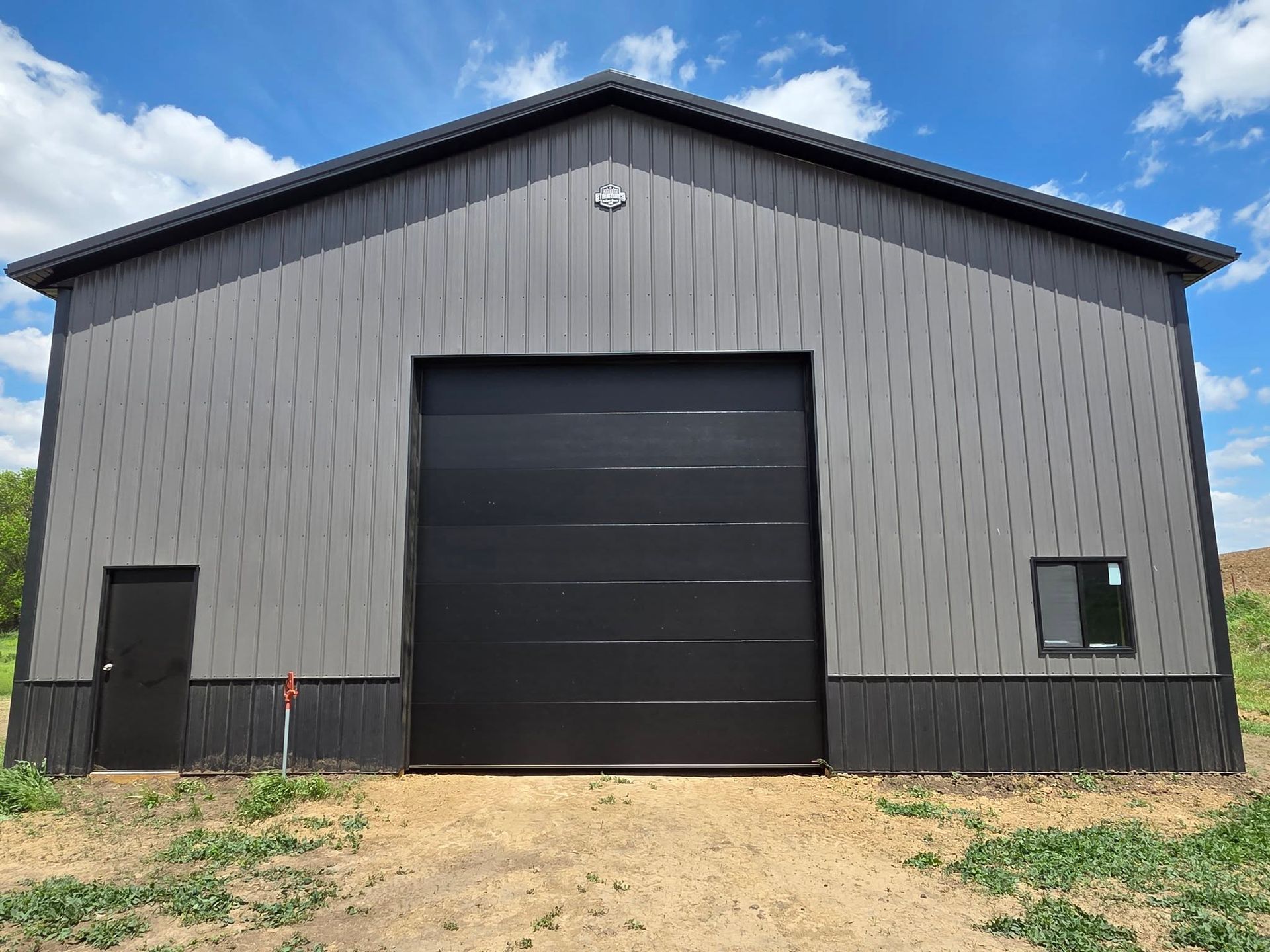 Gray and black metal building with large door, small door, and window under a blue sky.