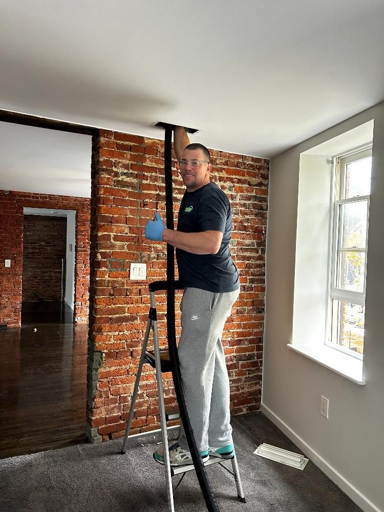 A man is standing on a ladder in a room with a brick wall.