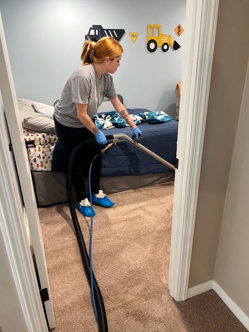 A woman is cleaning a carpet in a bedroom with a vacuum cleaner.
