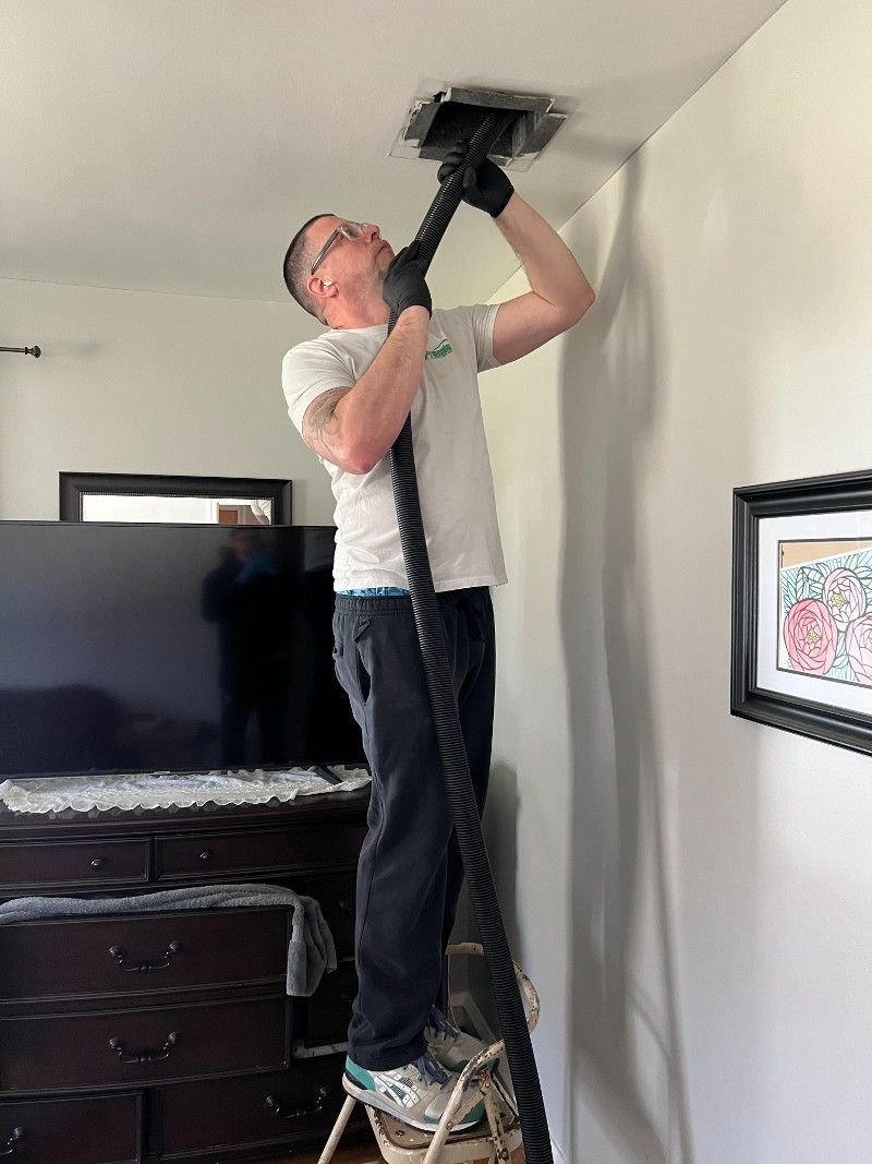 A man is using a vacuum cleaner to clean the ceiling of a living room.