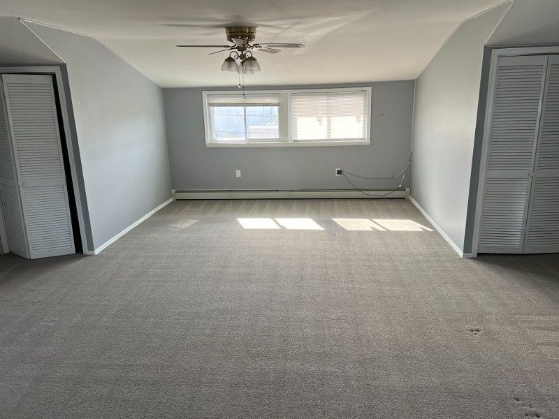 An empty living room with a ceiling fan and a lot of windows.