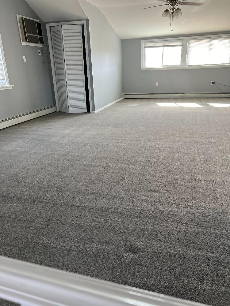 An empty room with a large carpeted floor and a ceiling fan.