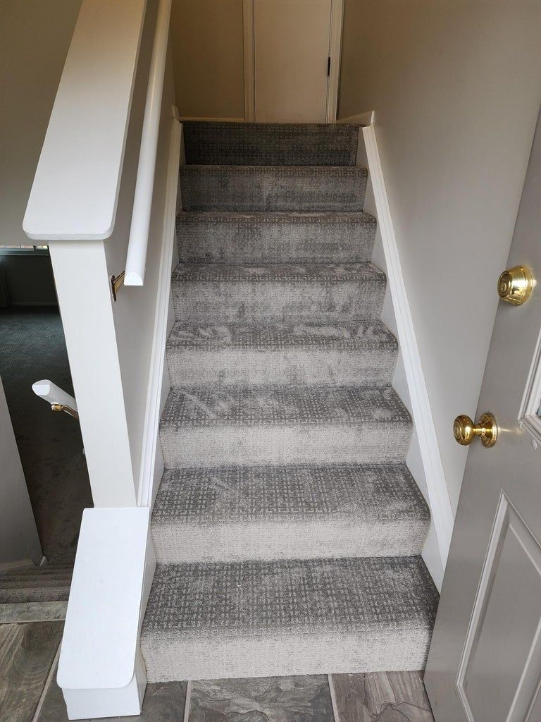 A set of stairs with a gray carpet and a white railing in a house.