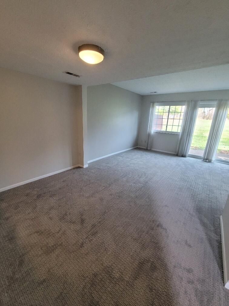 An empty living room with a gray carpet and a light on the ceiling.