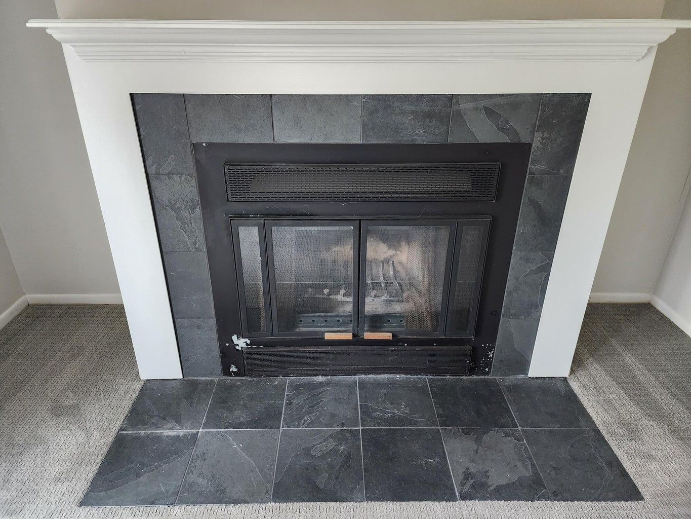 A fireplace with a black tile surround and a white mantle in a living room.