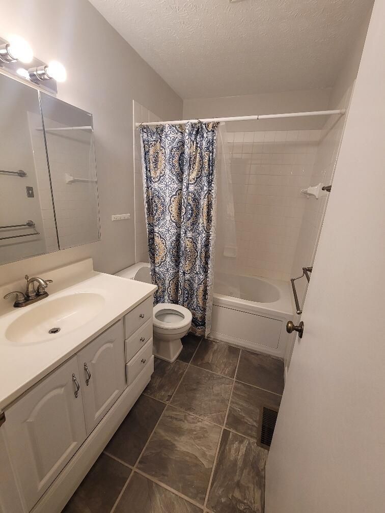 A bathroom with a toilet, sink, shower and mirror.