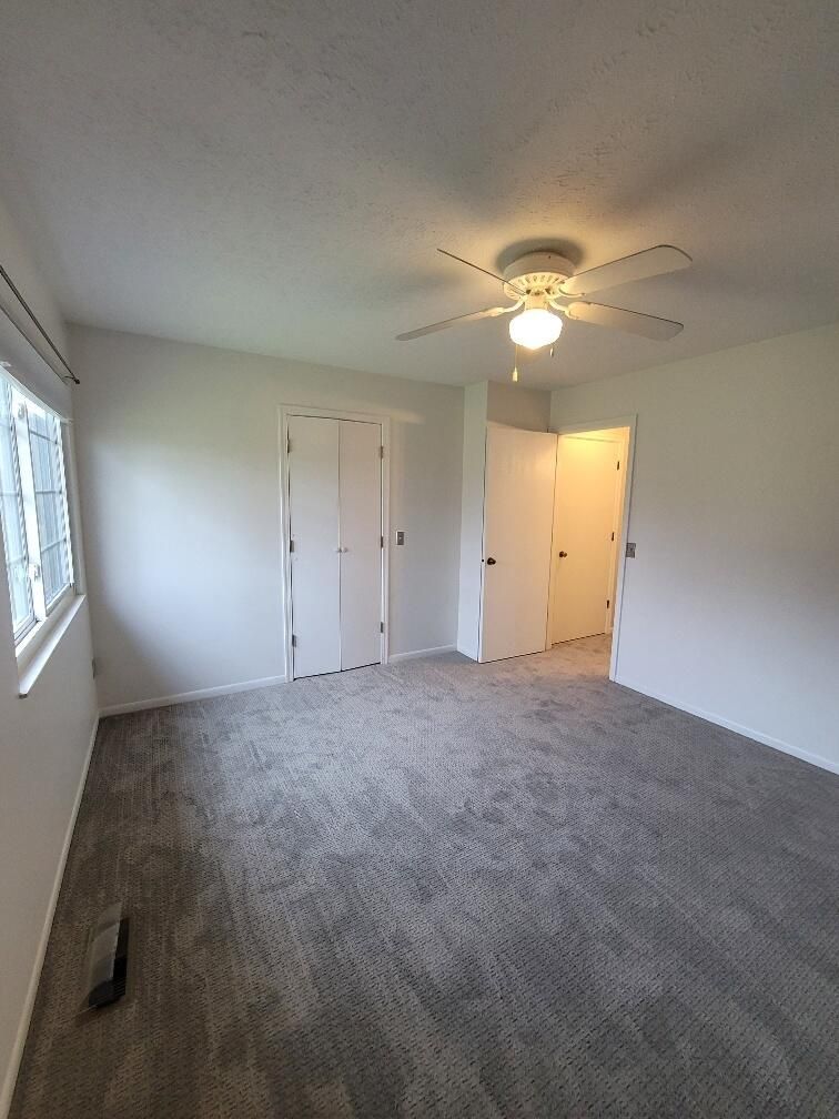 An empty bedroom with a ceiling fan and a window.