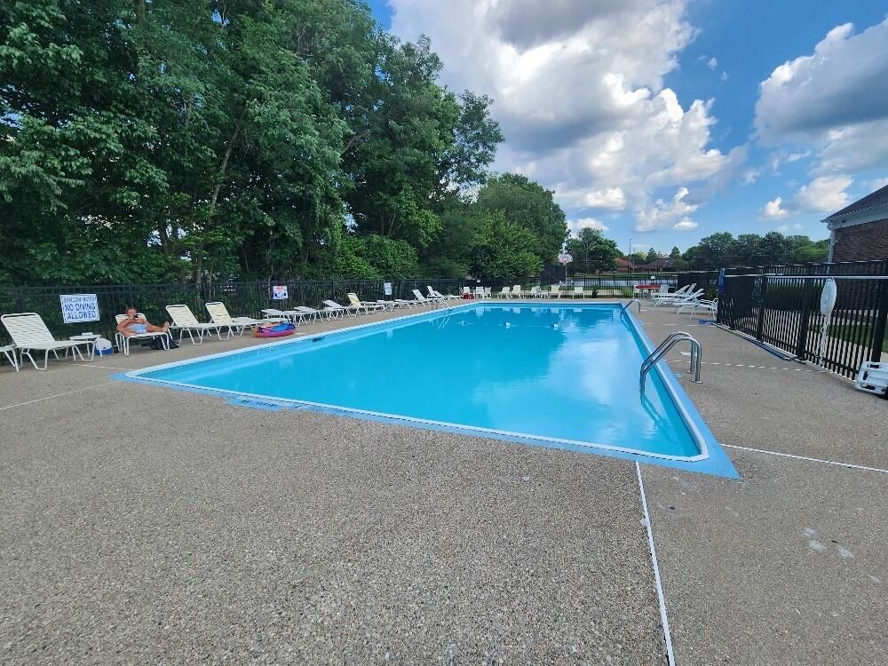 A large swimming pool surrounded by chairs and trees on a sunny day.