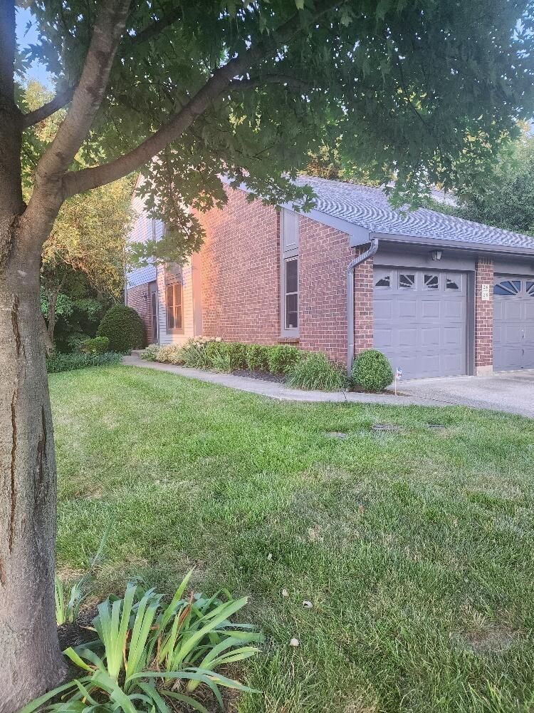 A brick house with two garage doors and a tree in front of it.