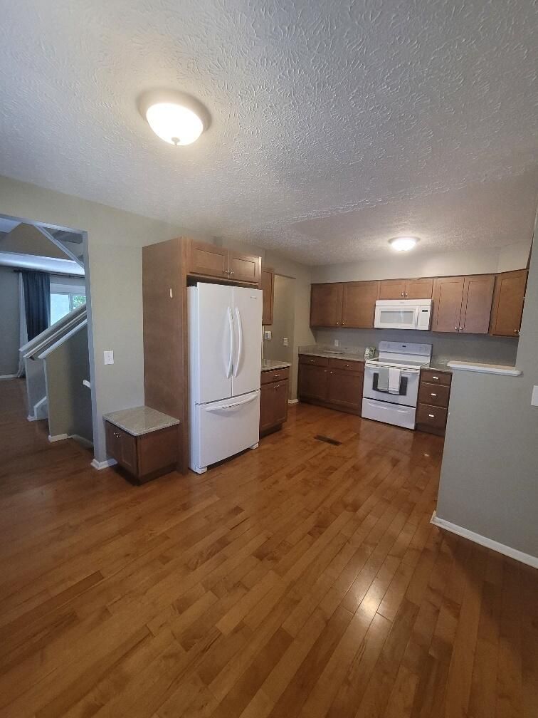 A kitchen with hardwood floors, a refrigerator, stove and microwave.