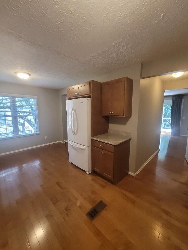 An empty kitchen with hardwood floors and a refrigerator.