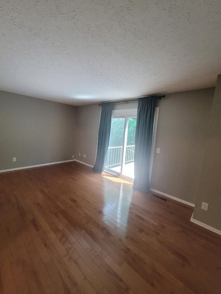 An empty living room with hardwood floors and a sliding glass door.