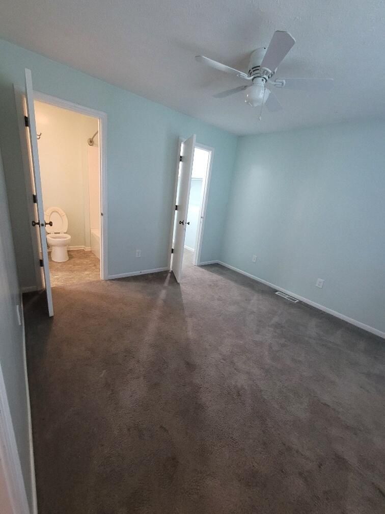 An empty bedroom with a ceiling fan and a toilet.