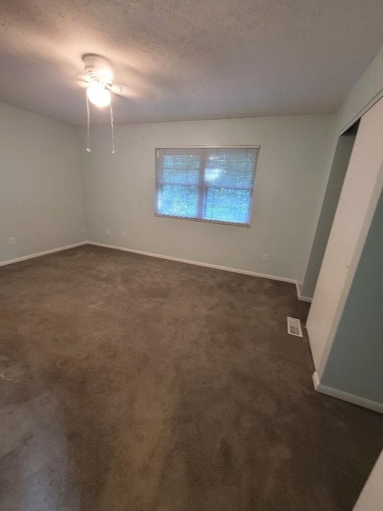 An empty living room with a ceiling fan and a window.