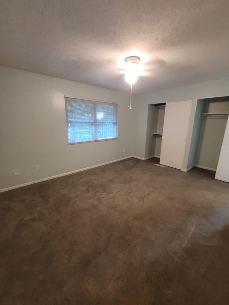 An empty bedroom with a ceiling fan and a window.