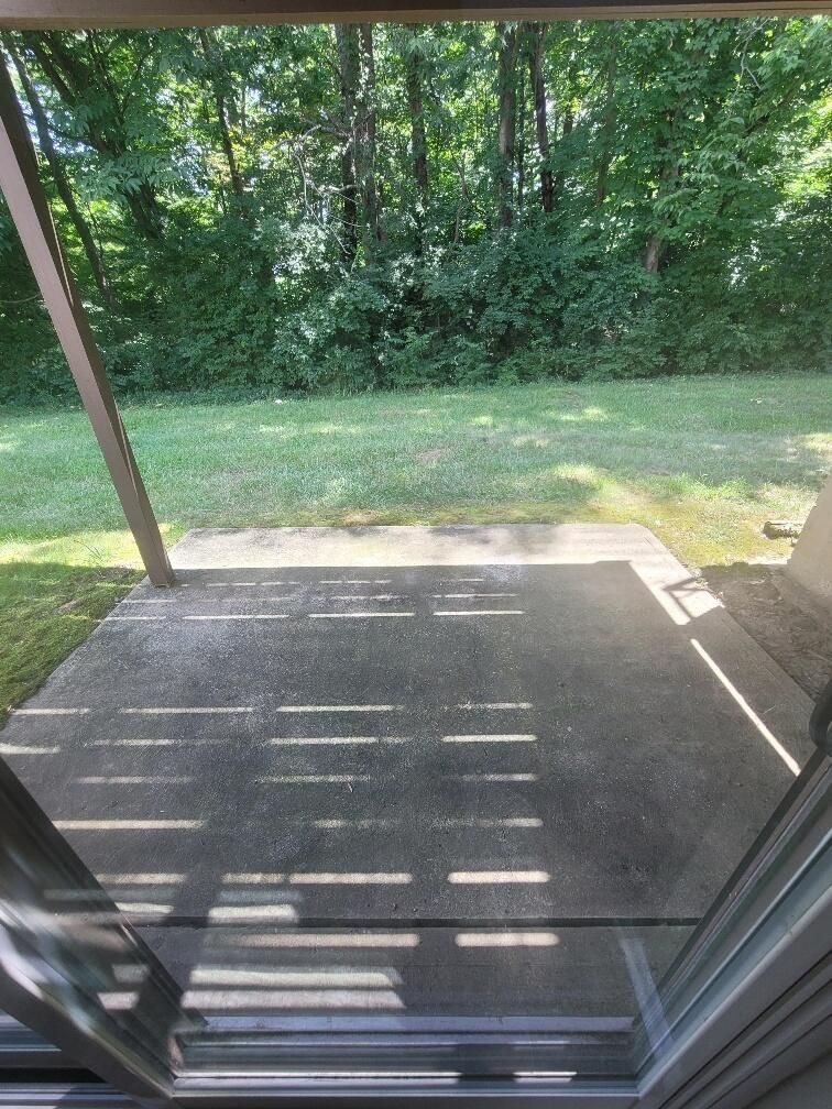 A view of a patio from a screened in porch with trees in the background.