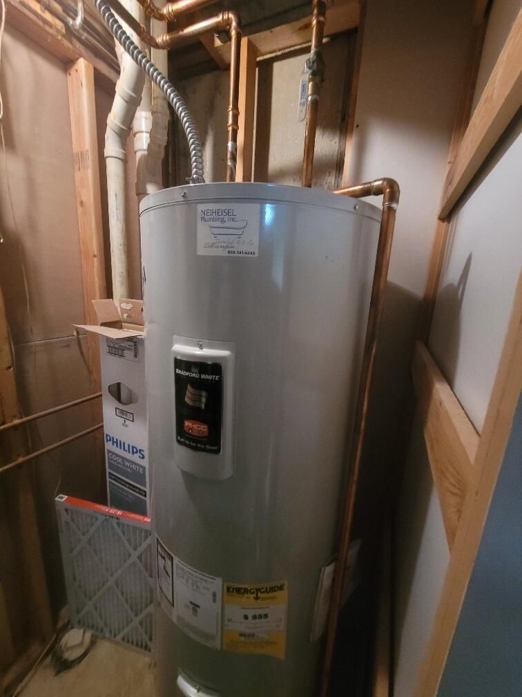 A water heater is sitting in a basement next to a box.