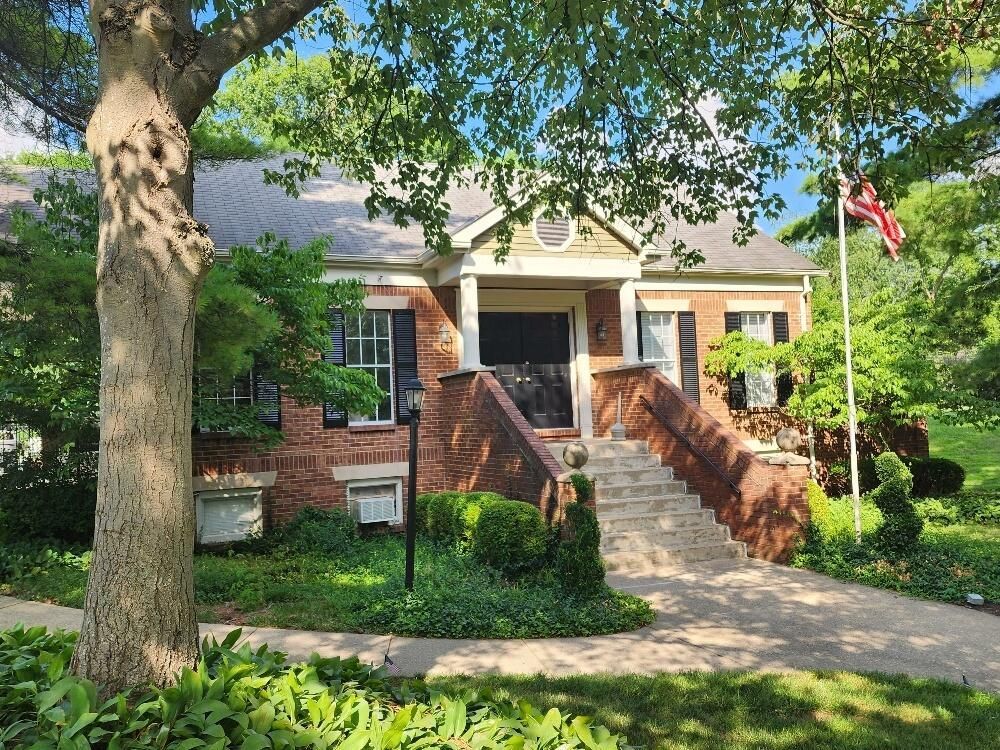 A brick house with stairs leading up to the front door and a tree in front of it.