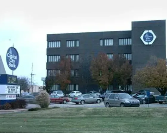 Capital City Bank building with sign, cars in parking lot, and cloudy sky.