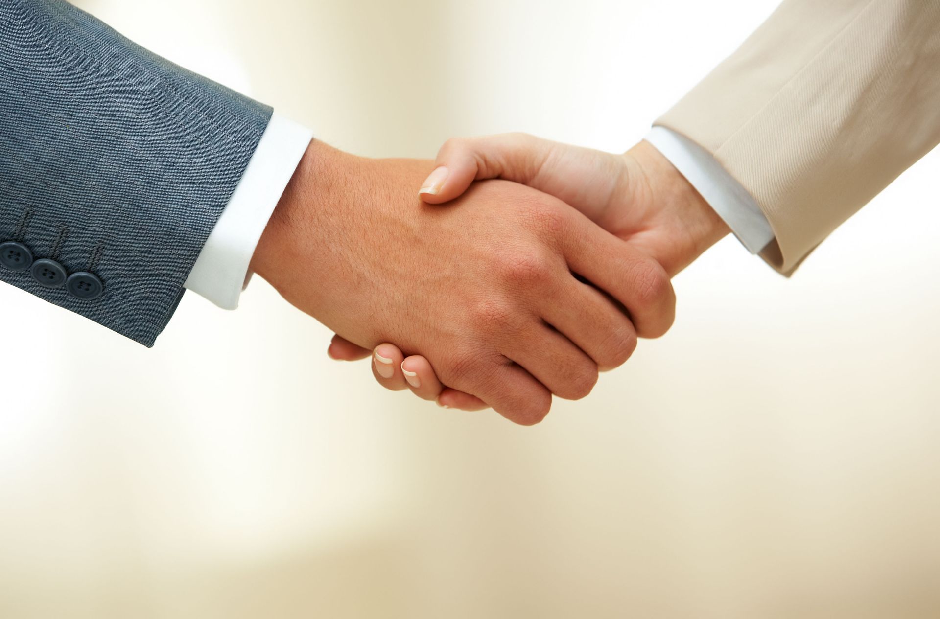 Two people shaking hands, business setting. One in gray suit, the other in tan.