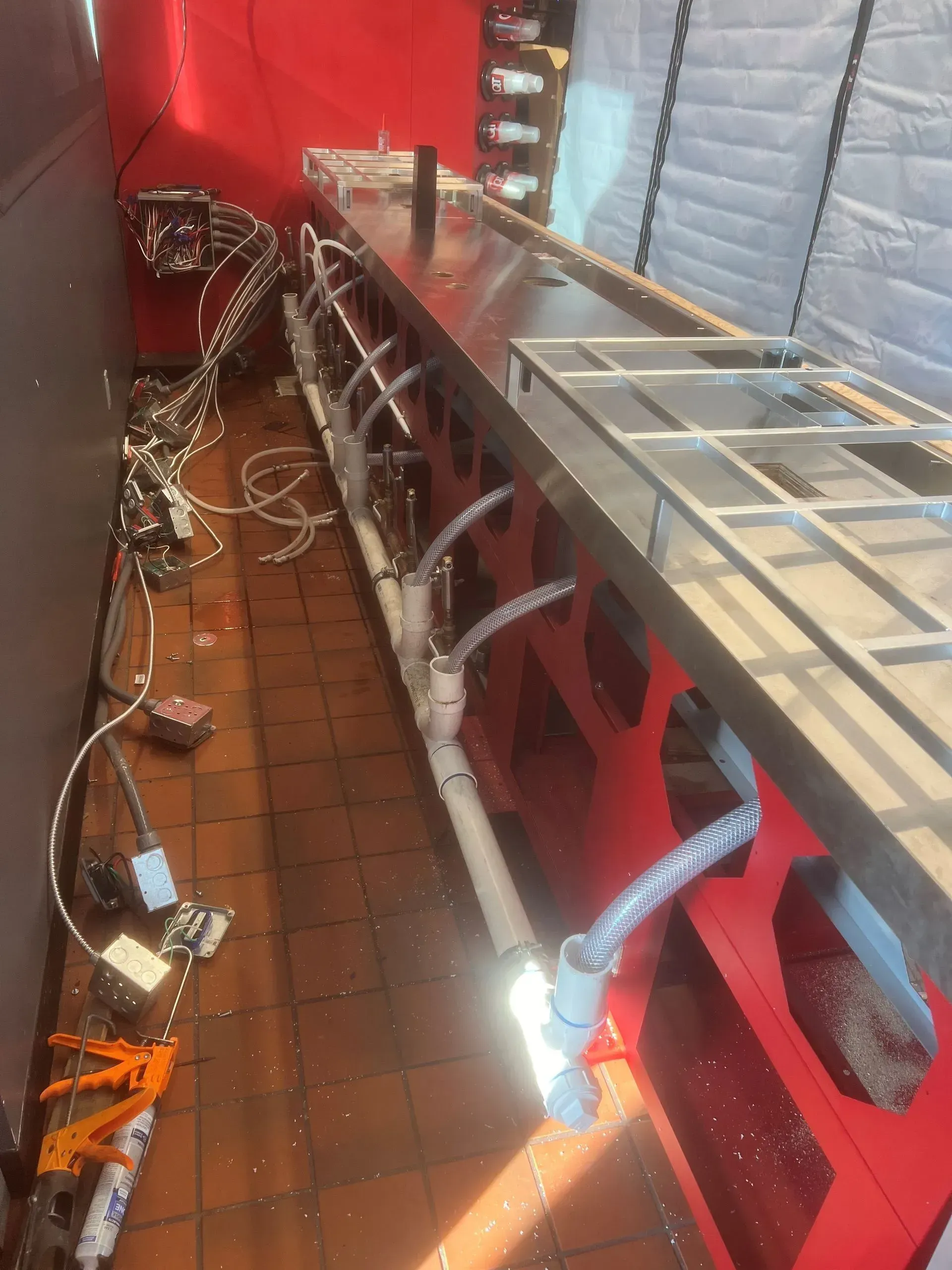 Red bar under construction with pipes, wires, and unfinished shelving. Floor is tile, and walls are red and gray.