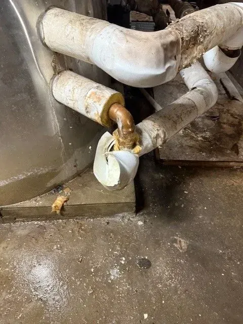 Pipes with worn insulation, showing exposed metal, in a basement setting with concrete floor and debris.