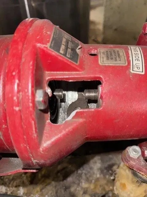 Red industrial pump, revealing internal components through an opening. The setting appears to be a utility room.