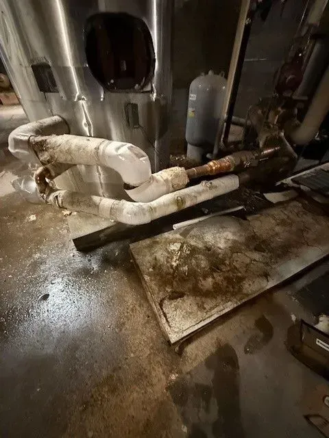 Basement flooded with water and debris; damaged pipes with insulation, near a water heater.