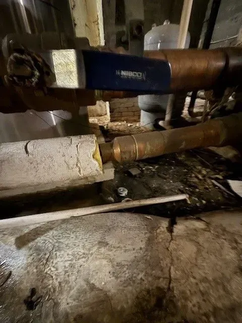 Copper pipes with a valve in a basement setting, covered in insulation and debris.