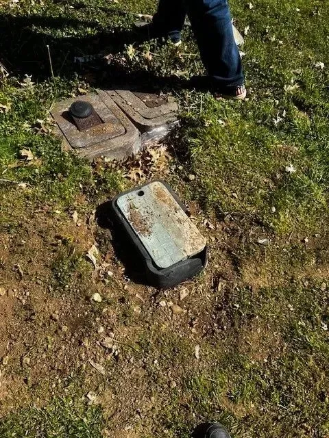 A person standing near an open, rusted utility box in a grassy yard.