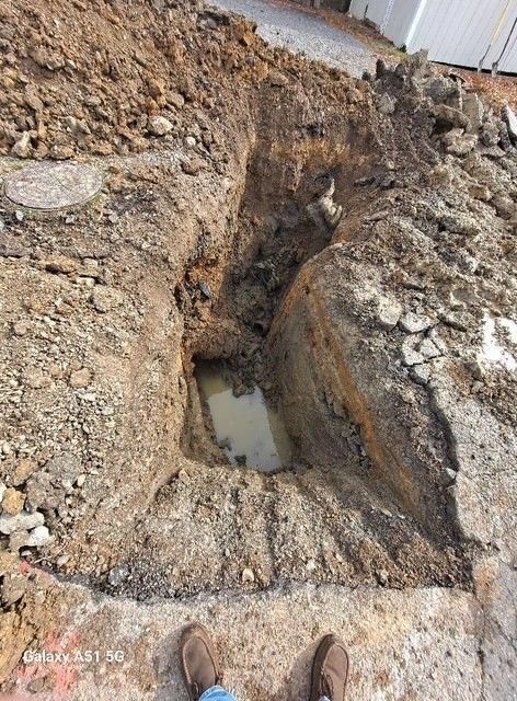 A muddy pit with water inside. A person's feet are visible at the bottom.