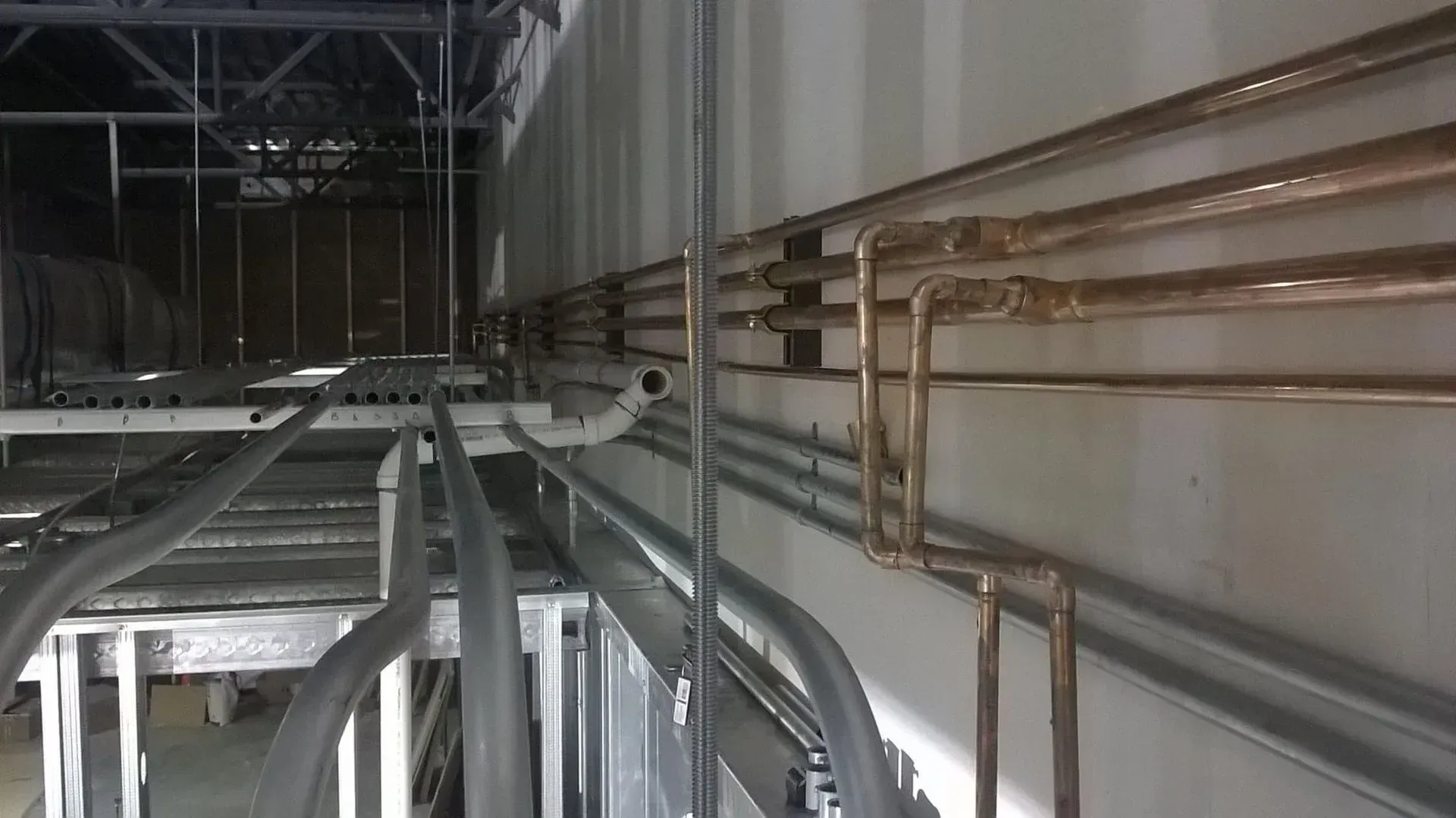 Electrical and plumbing infrastructure, including conduit and copper pipes, in a building under construction.