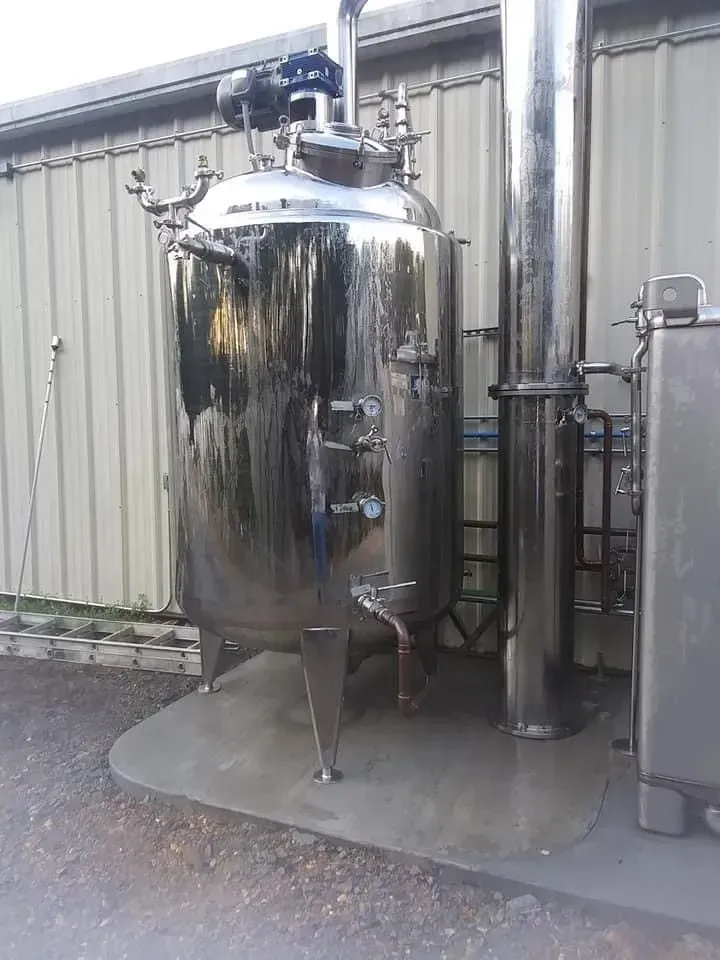 Large, shiny, stainless steel industrial tank outside against a corrugated metal building.