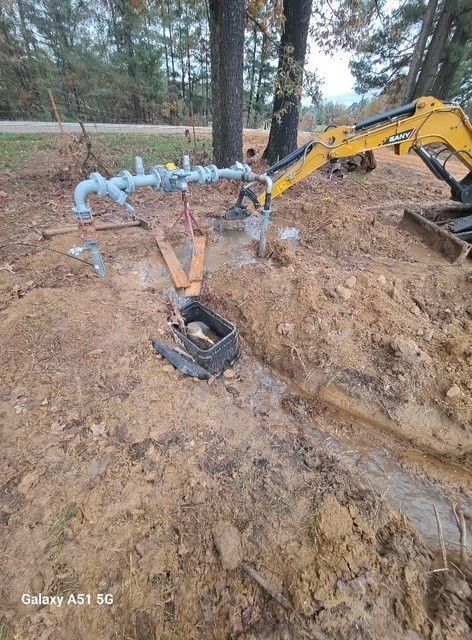 Excavation site with exposed gas pipes, a backhoe, and a broken utility box.