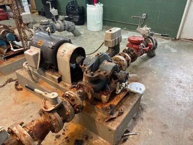 Rusty water pump system with pipes, valves, and an electric motor, indoors.