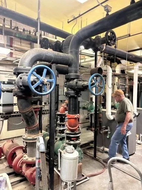 Man in blue jeans near industrial pipes and valves in a utility room.