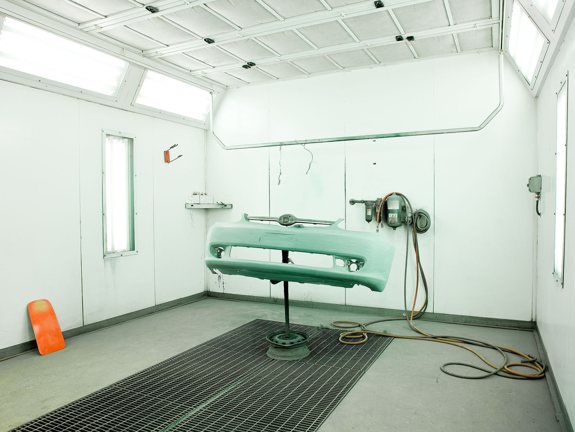 A car bumper on a stand in a white paint booth.