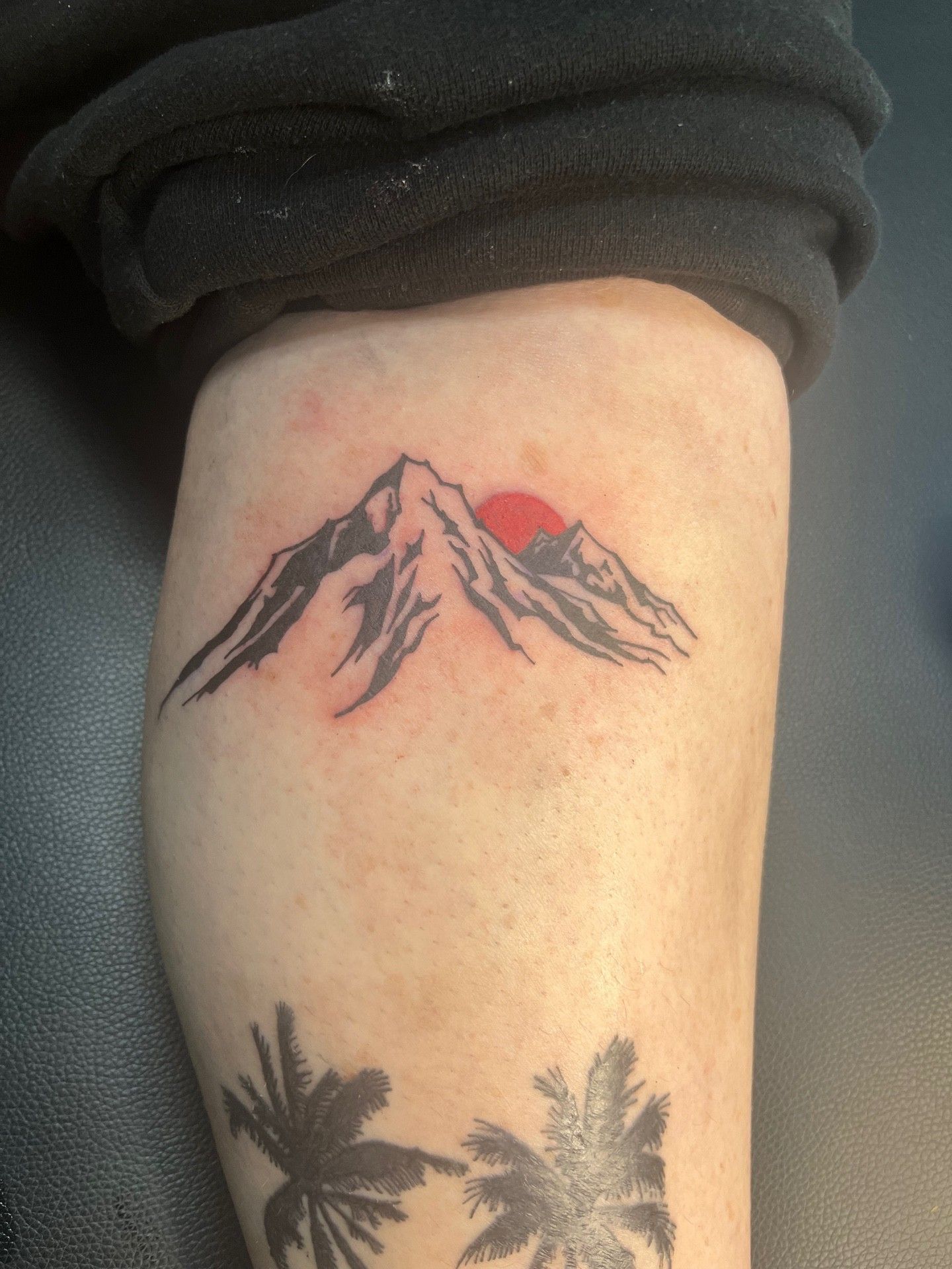 A tattoo of a mountain with the sun behind it