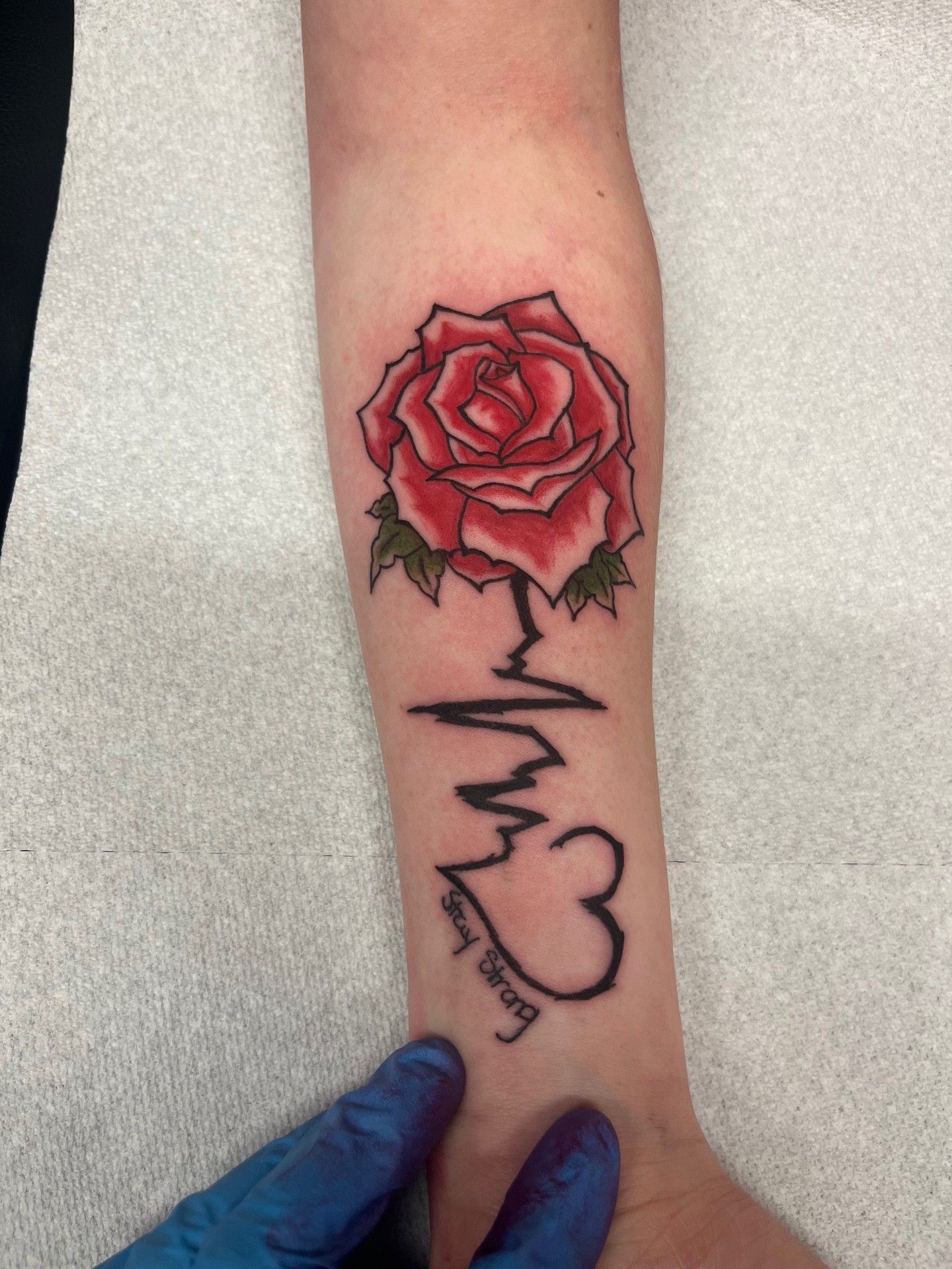 A person has a tattoo of a heartbeat and a rose on their forearm