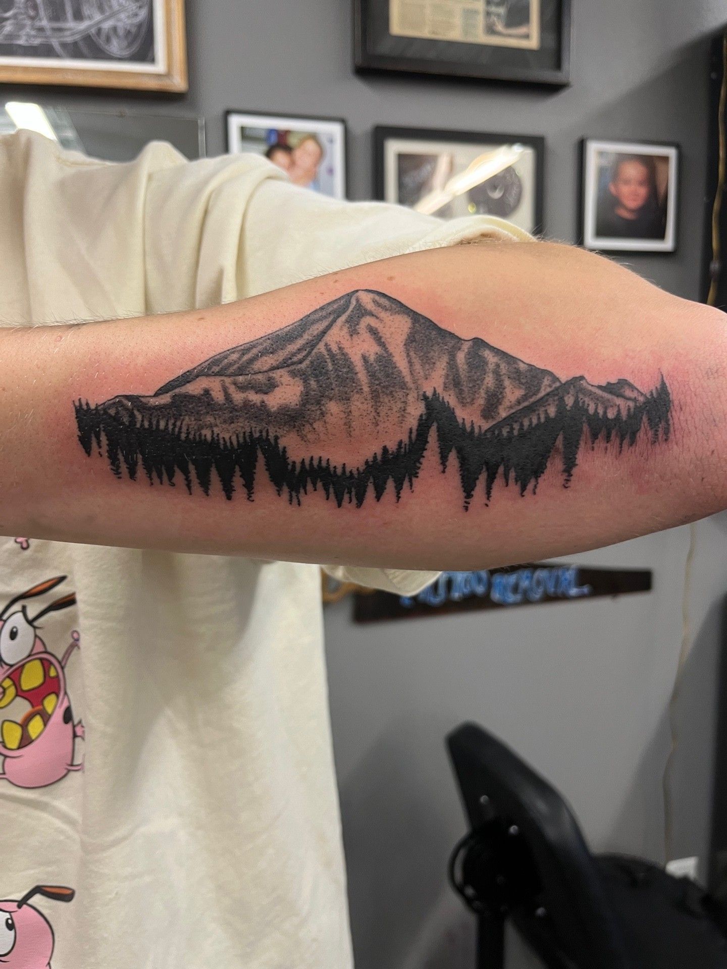 A person has a tattoo of a mountain and trees on their forearm.