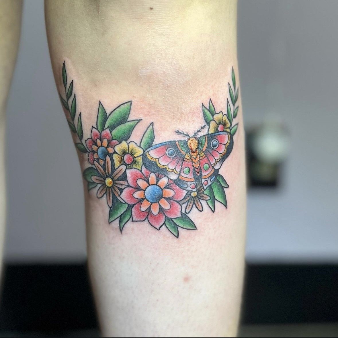 A woman has a tattoo of a butterfly surrounded by flowers on her leg