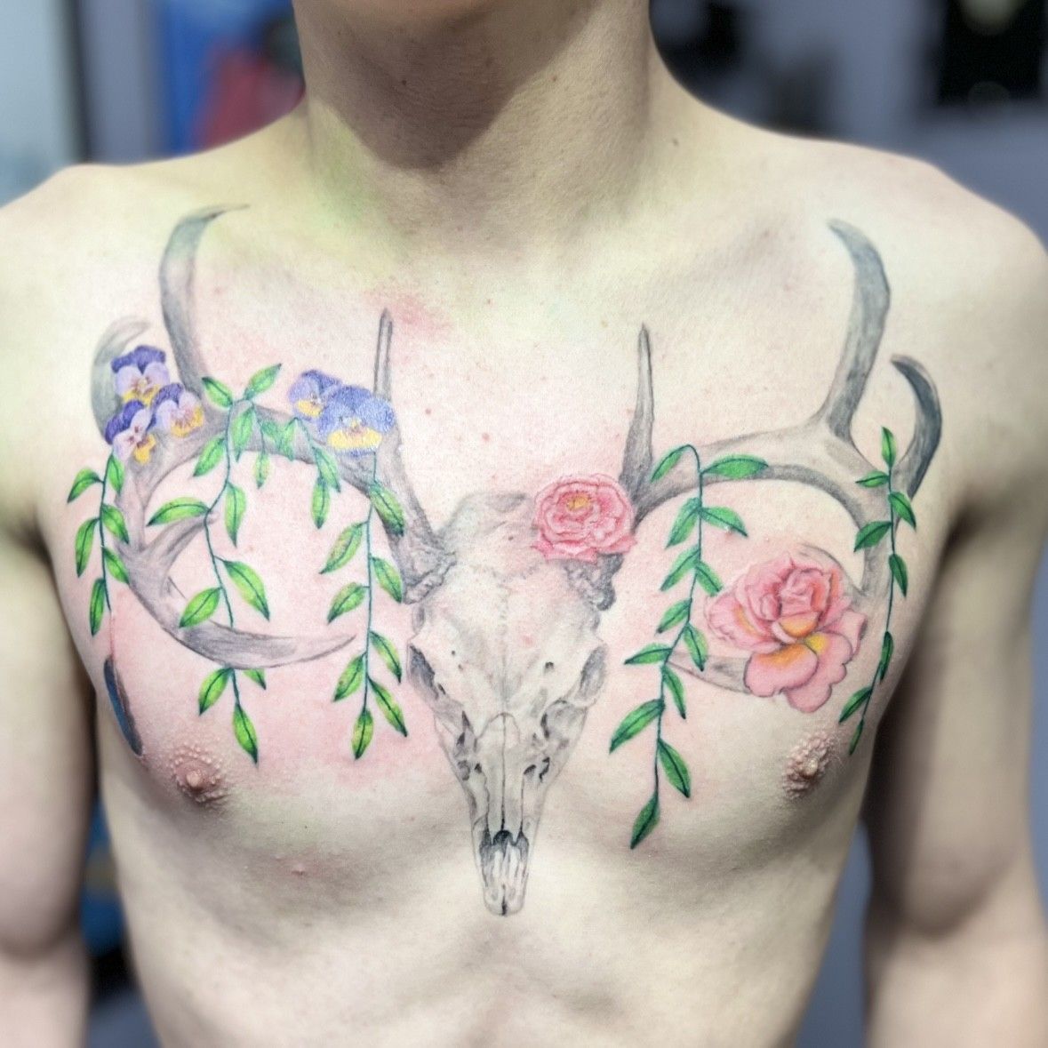 A man has a tattoo of a deer skull with antlers and flowers on his chest