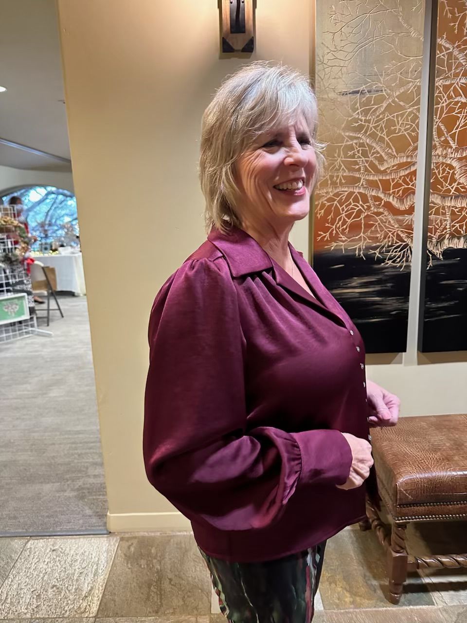 A woman in a maroon shirt is smiling in a room.