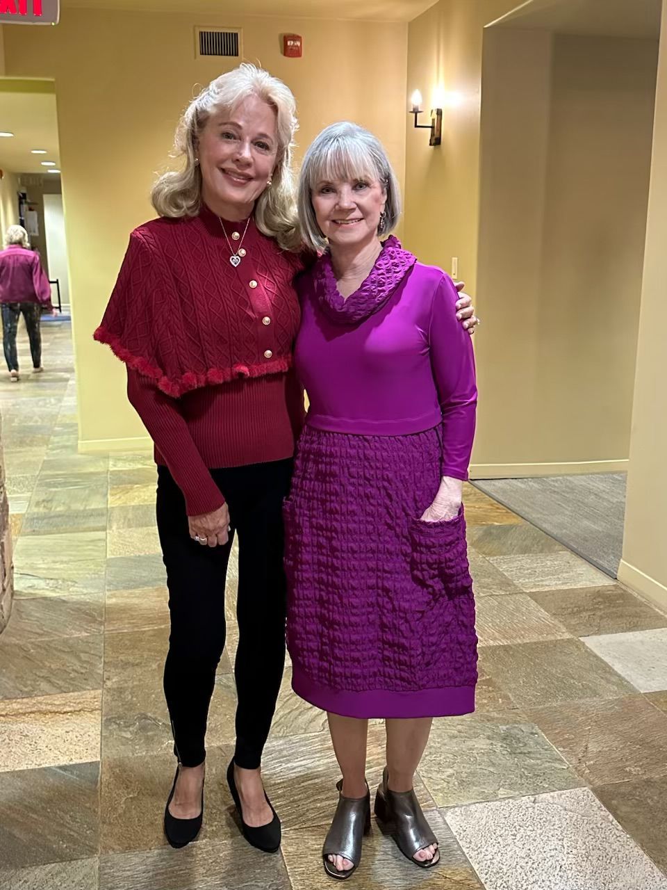 Two women are standing next to each other in a hallway.