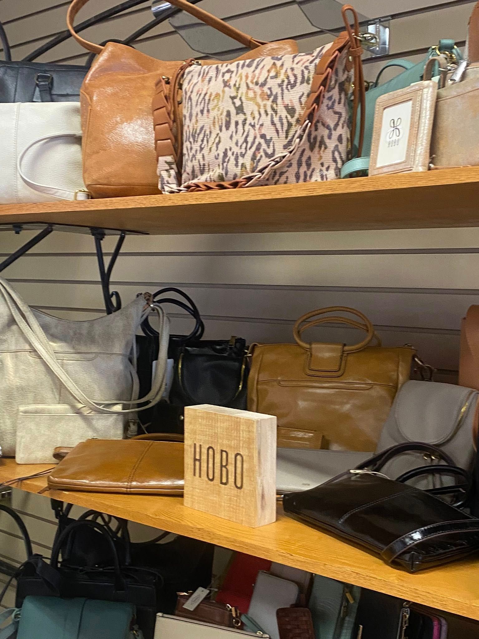 Bags on display on shelves in a store. Includes brown, tan, leopard print, and black bags.