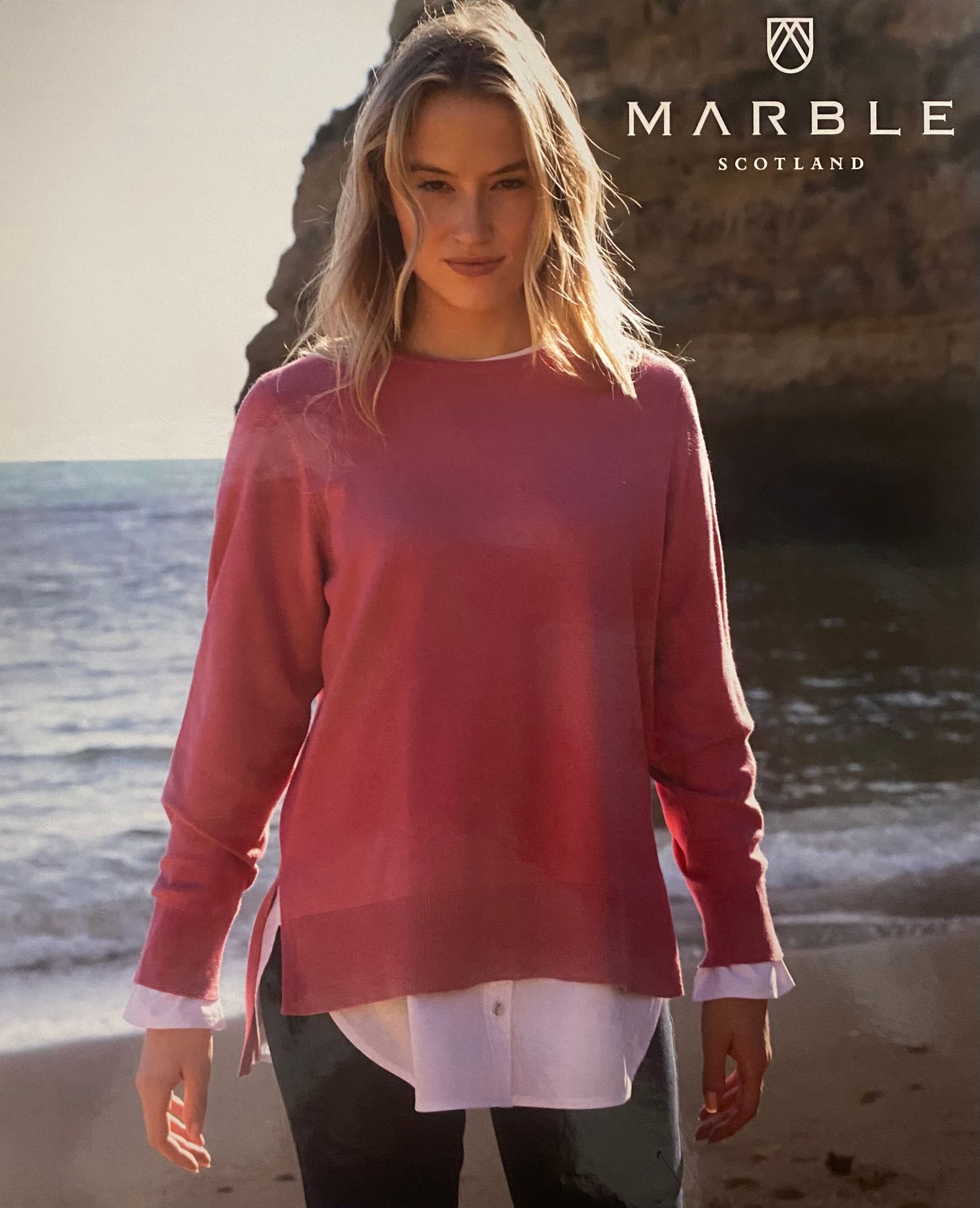 Woman in pink sweater and white shirt at the beach.
