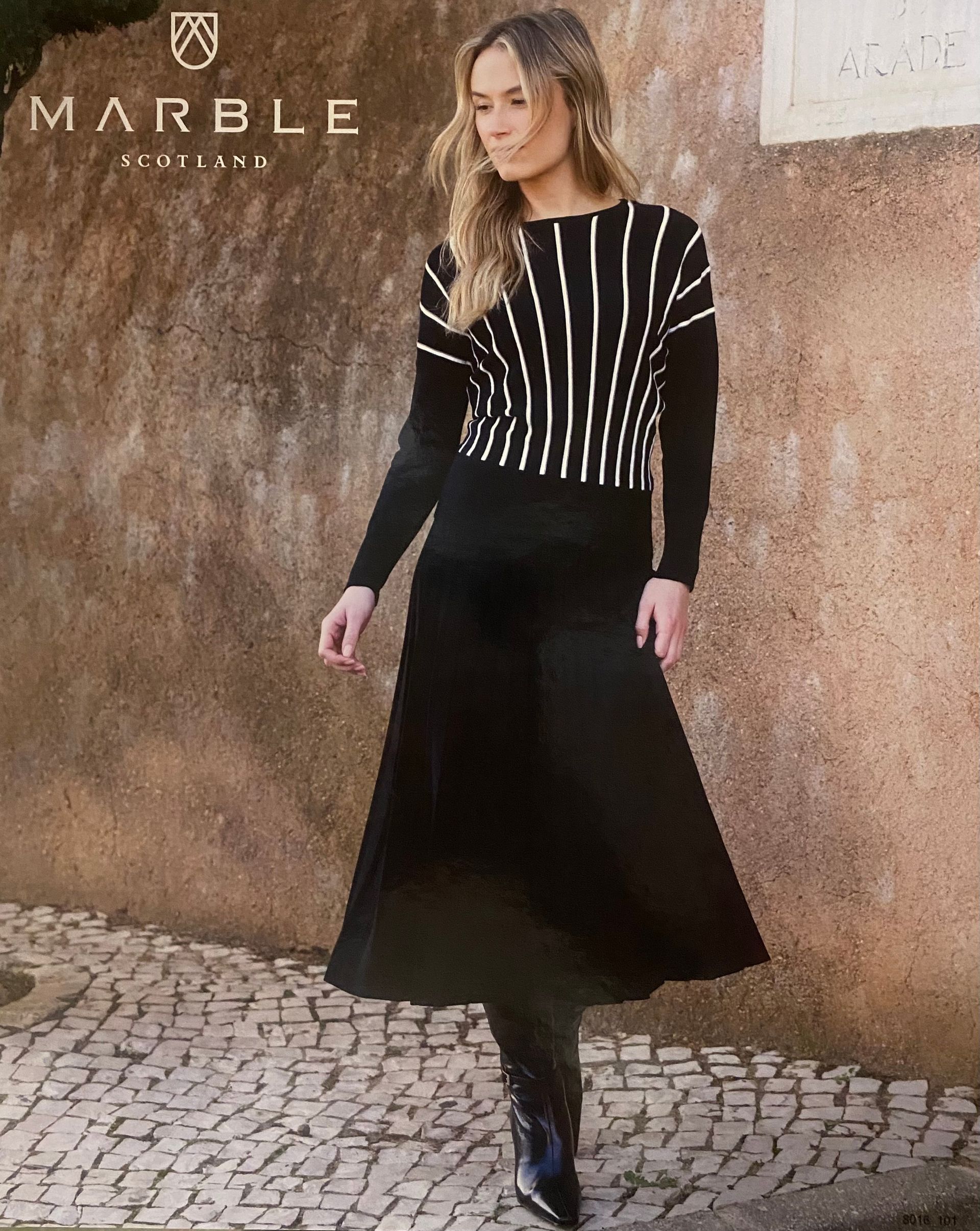 Woman in black and white striped sweater, black skirt, standing outdoors.