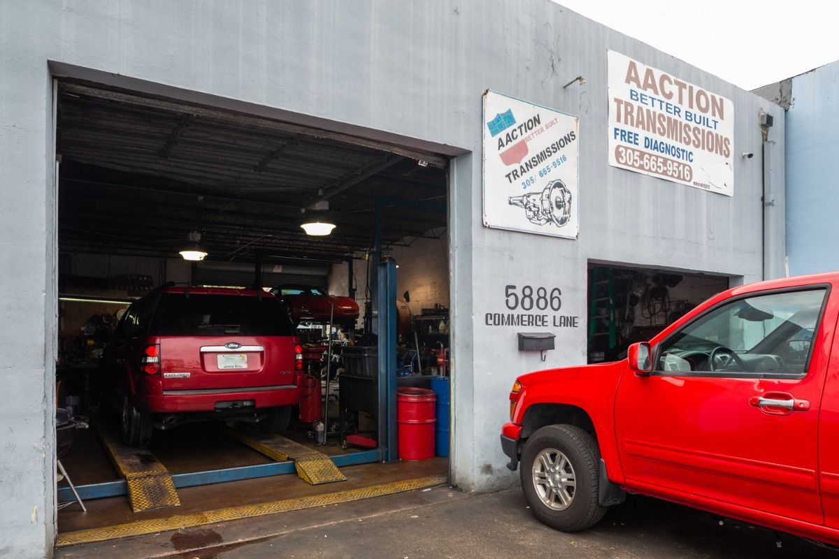 Red SUV inside an auto repair shop garage with another red truck parked outside.
