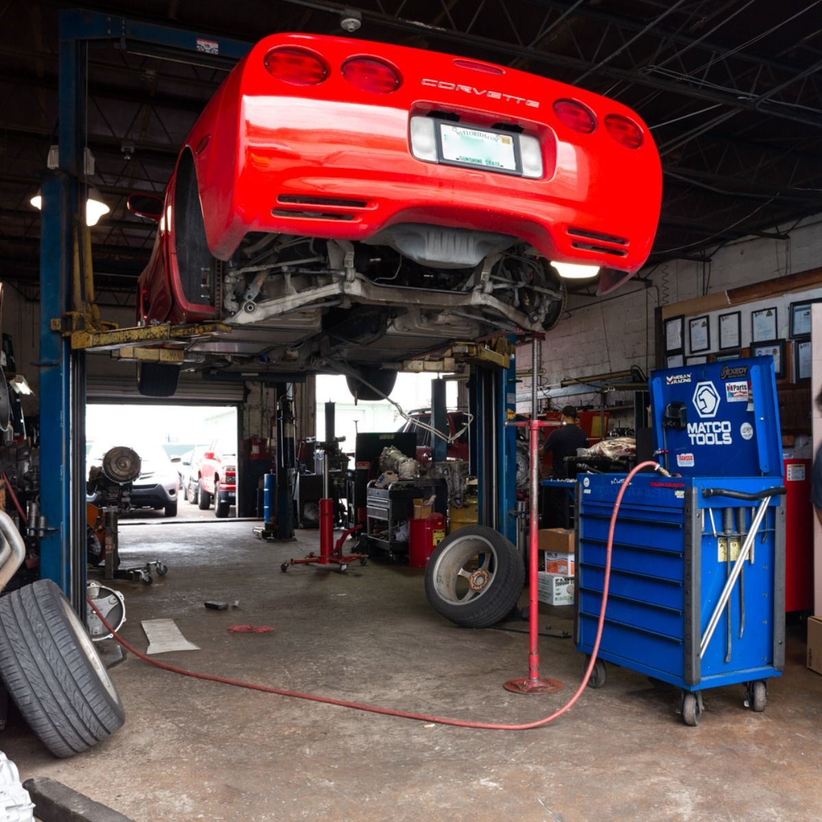 Red sports car lifted on a garage hoist, with tools and equipment in an auto repair shop.
