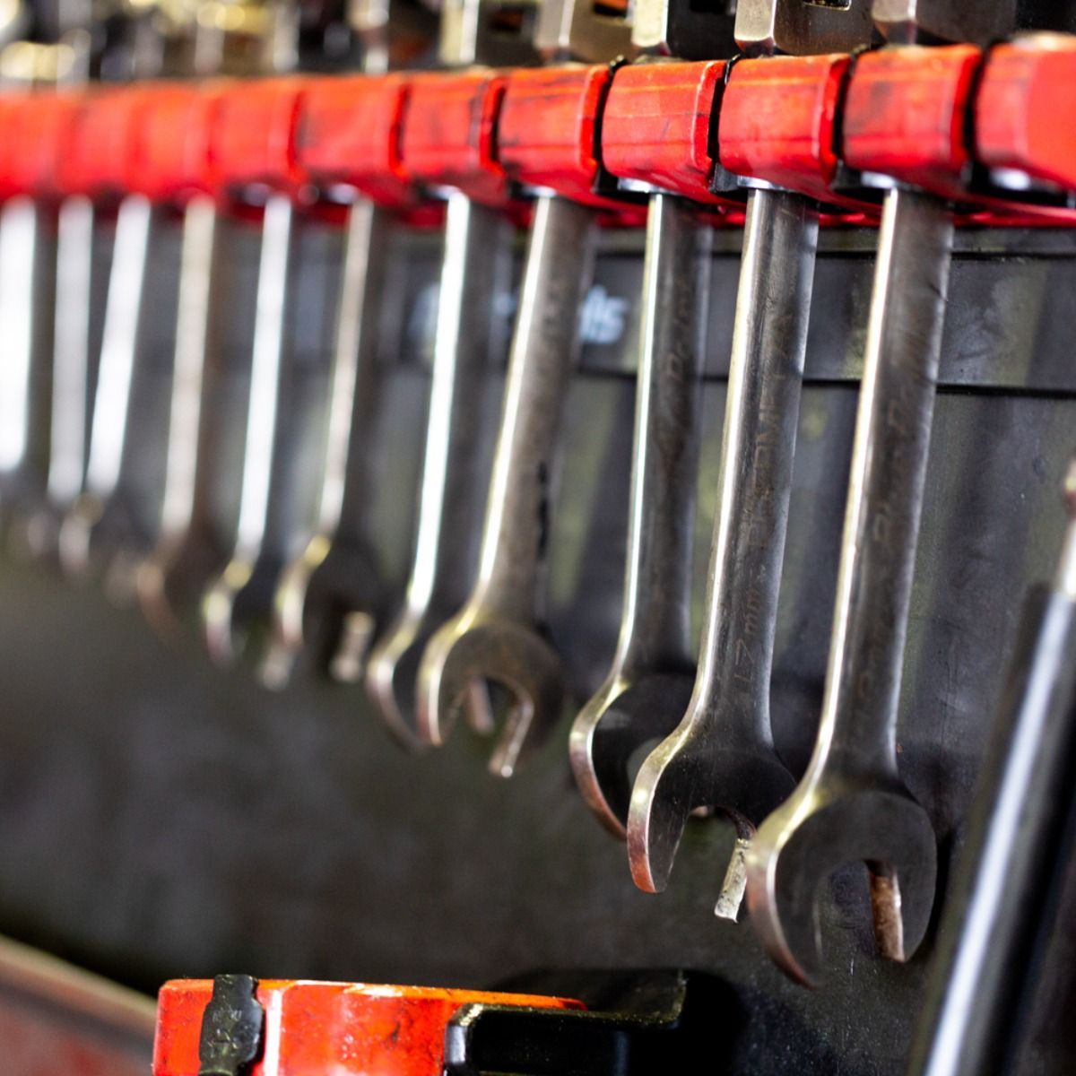 Row of red-handled wrenches hanging on a tool rack in a workshop